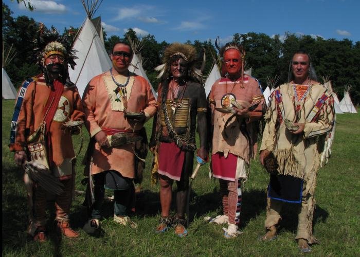 Fünf Mitglieder in Kleidung der Plains-Stämme vor Tipis